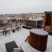 Dachterrasse mit Polar Spa Standard Eisbad aus Thermoholz und Whirlpool, dahinter Liegestühle und Stadtblick
