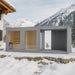 Moderne Gartensauna Tauras Balance in grauem Holzdesign neben einer Chalet-Villa im verschneiten Skigebiet, umgeben von Alpenpanorama und winterlicher Naturkulisse – stilvolle Outdoor-Wellness im Schnee.