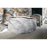 Graue Naturstein-Badewanne mit strukturierter Oberfläche vor rustikaler Steinmauer in Außenumgebung