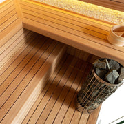 Detailaufnahme der AWT E1601C Sauna mit Sitzbank aus roter Zeder, Bodenrost und Saunaofen mit Steinen