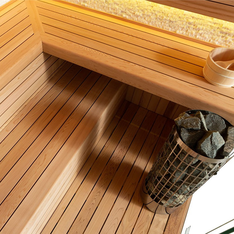 Detailaufnahme der AWT E1601C Sauna mit Sitzbank aus roter Zeder, Bodenrost und Saunaofen mit Steinen