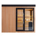 Frontansicht der AWT The Cube X7-L Hemlock Außensauna 300×235 cm mit EOS BiO-Cubo Ofen, Glasfront und warmer gelber LED-Ambientebeleuchtung