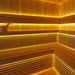 Eckansicht der AWT The Cube X7-L Hemlock Außensauna 300×235 cm mit zweistufigen Bänken, Aufgusskübel und warmer gelber LED-Ambientebeleuchtung