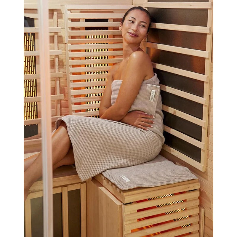 Frau sitzt entspannt auf Badesofa Sitzkissen und Saunatuch in Taupe – weiches Sauna-Set aus Bio-Baumwolle