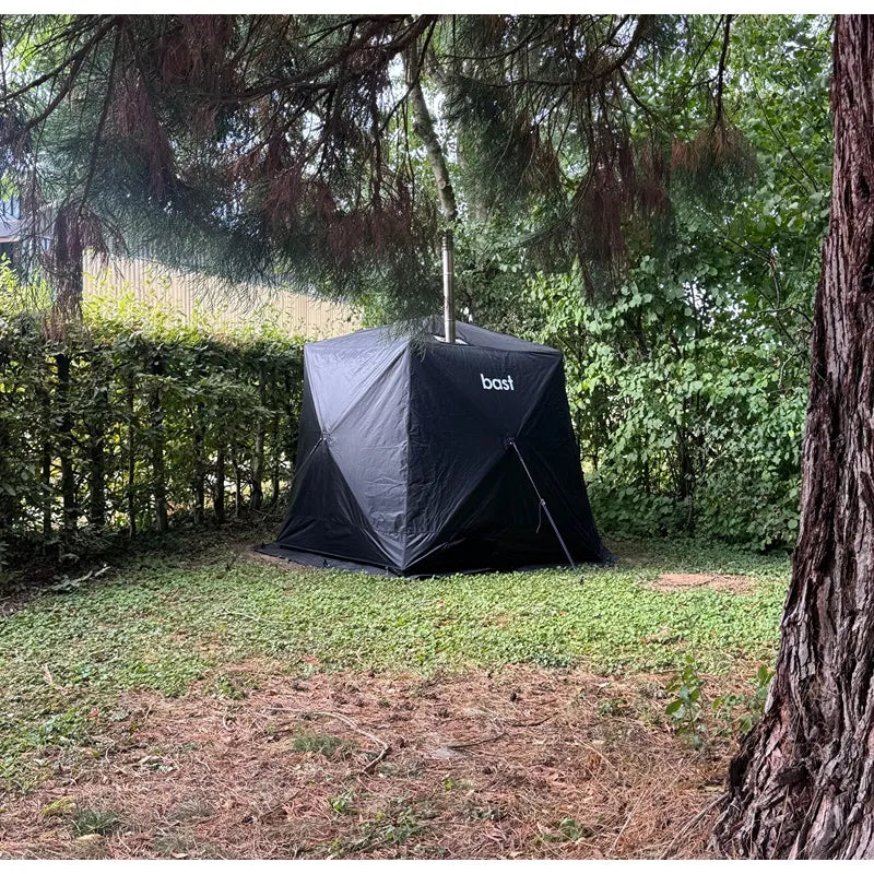 Bast Björk Deluxe Zeltsauna schwarzes Zelt im Garten zwischen Bäumen aufgestellt