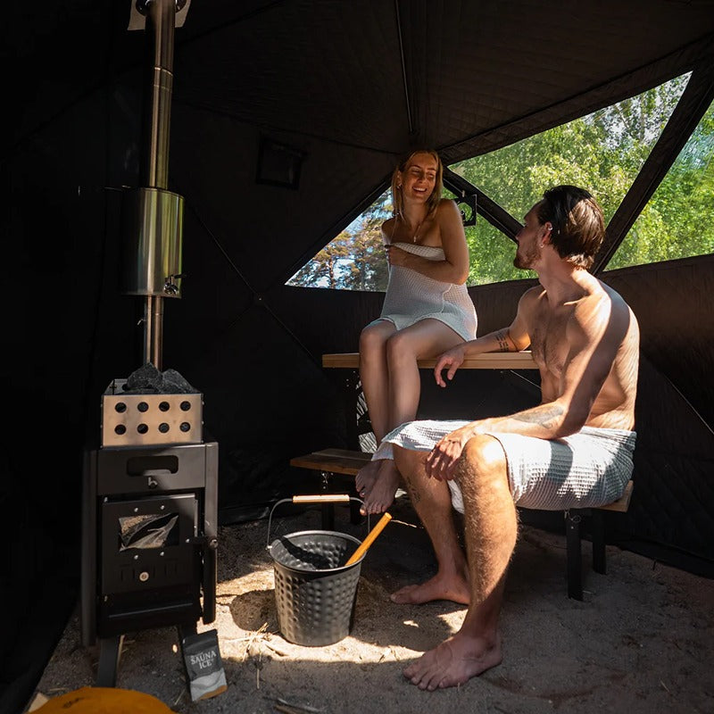 Innenansicht der Bast Näver Deluxe Zeltsauna mit zwei Personen auf Sitzbänken und aktivem Saunaofen