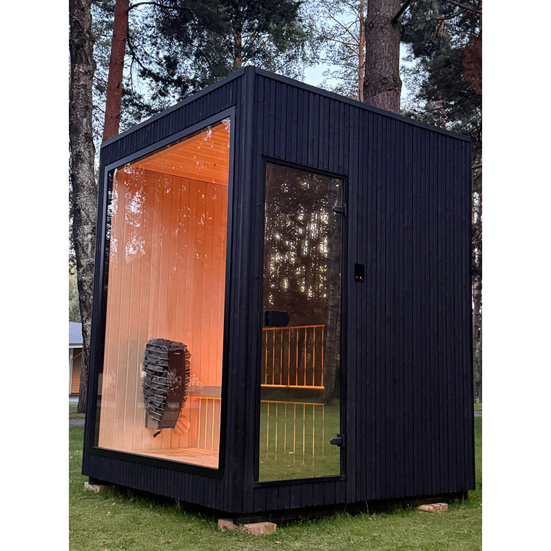 Schwarze Premiumsauna Jonas Small mit rahmenloser Glasfront und Glastür, beleuchtet, freistehend im Waldgebiet.