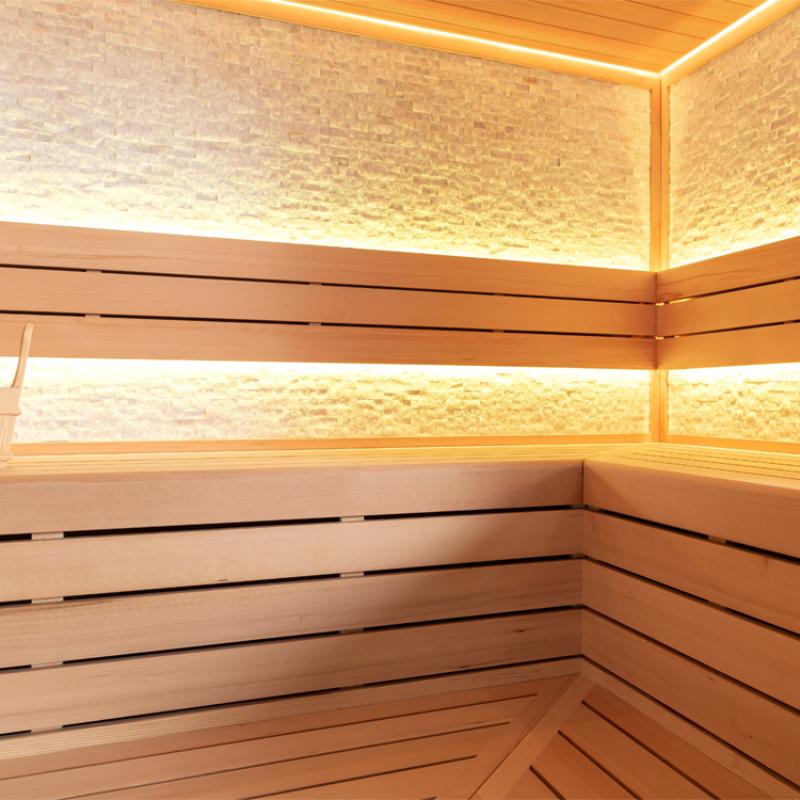 Modernes Saunainneres mit Holzbänken in Hemlock-Holz, indirekter LED-Beleuchtung und strukturierter Rückwand, ideal für 3-4 Personen