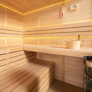Modernes Inneres einer Holzsauna mit Hemlock-Holzverkleidung, zwei L-förmigen Sitzbänken, warmweißer LED-Beleuchtung, Hygrometer, Saunaeimer und Kelle, ideal für 4+ Personen.