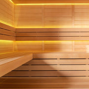 Innensicht einer Holzsauna mit Hemlock-Holzverkleidung, mehreren Sitzbänken und warm-gelblicher LED-Beleuchtung oben an den Wänden