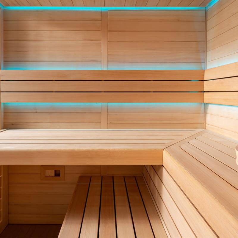 Innenansicht einer modernen Infrarotsauna aus Hemlock-Holz mit türkisen LED-Lichtelementen, zwei Liegen und ergonomischen Rückenlehnen