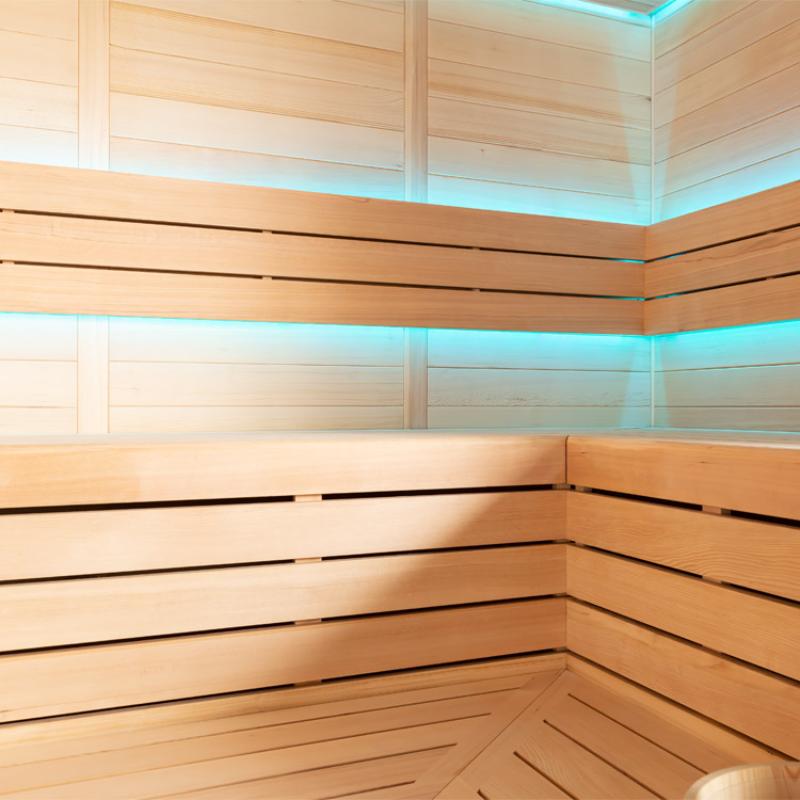 Modernes Saunainneres mit hellem Hemlock-Holz, mehrstöckigen Sitzbänken und türkisfarbener LED-Beleuchtung an Decke und Wänden
