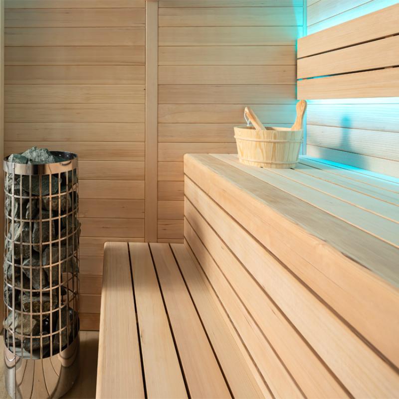 Modernes Saunainterior mit Holzbanken, Saunaofen mit Steinen und Holzeimer, blaue LED-Beleuchtung an der Wand