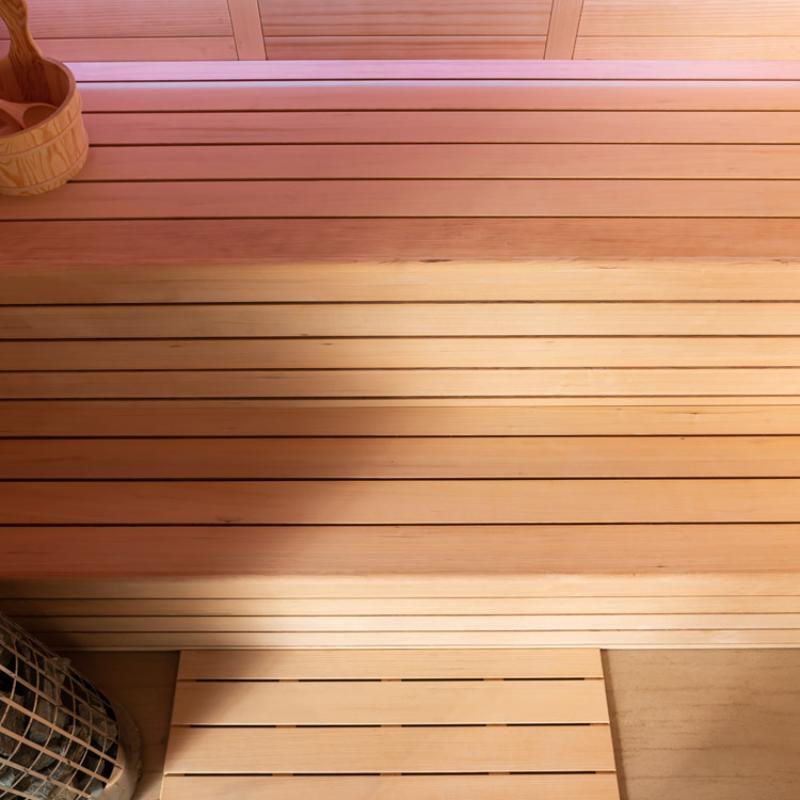 Innenansicht einer Hemlock-Sauna mit hellen Holzbänken, dimmer LED-Beleuchtung oben und Saunazubehör seitlich, EAGO AWT E1614C Modell