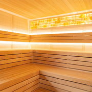 Modernes Saunainnenraum mit heller Hemlock-Holzverkleidung, integrierter LED-Beleuchtung in zwei Ebenen und geräumigen Sitzbänken für mehrere Personen.