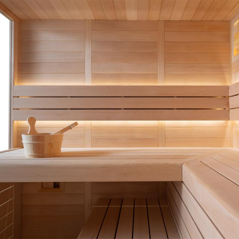 Moderne Holzsauna mit Hemlock-Holz, heller Innenausstattung, LED-Beleuchtung und Saunazubehör auf der Liegebänken