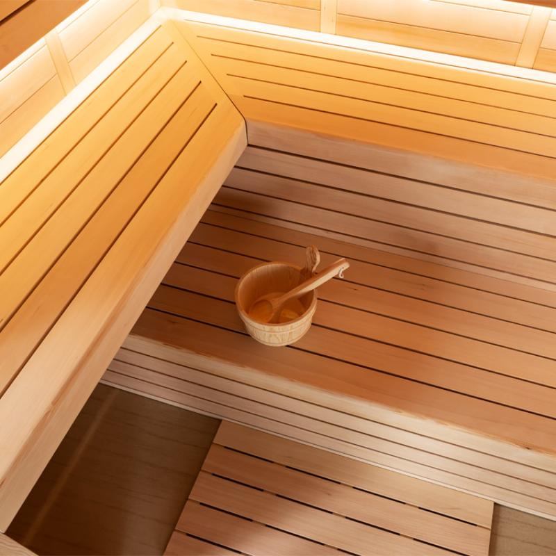 Innensicht einer Hemlock-Sauna mit Holzbänken und traditionellem Saunaeimer auf der unteren Bank