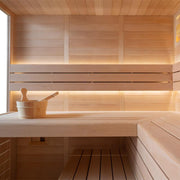 Modernes Saunainterieur aus hellem Holz mit Sitzbänken, Rückenlehnen mit indirekter LED-Beleuchtung und traditionellem Saunazubehör auf der Ablage