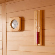 Saunaraum mit Holzwandverkleidung, an der eine runde Holzuhr und ein vertikales Holz-Thermometer mit roter Flüssigkeit hängen.