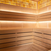 Modernes Saunainnenraum aus hellem Hemlock-Holz mit durchgehenden Bänken, indirekter LED-Beleuchtung und amber-farbenen Glaspanelen in der Decke