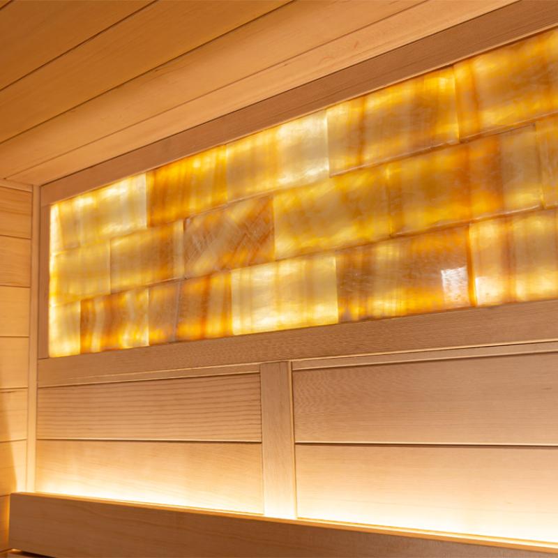 Innenaußsicht einer Hemlock-Sauna mit hellen Holzpaneelen, beleuchteten Glaseinsätzen in der oberen Wand und warmweißer LED-Beleuchtung an den Holzbänken.