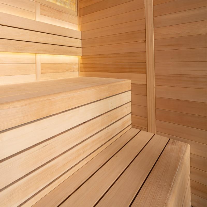 Modernes Saunainnenraum aus hellem Hemlock-Holz mit Sitzbänken, Rückenlehne und horizontalen Holzplanken an den Wänden sowie indirekter Beleuchtung