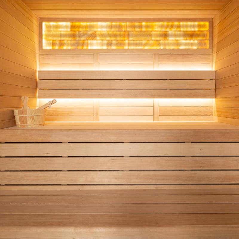 Innenansicht einer Hemlock-Sauna mit Infrarotstrahler oben und beleuchteten Holzbänken, Saunakübel und Kelle sichtbar