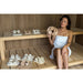Frau in Sauna mit Halu Sauna Round Kopfstütze aus Holz in der Hand – ergonomisches Saunazubehör für stilvolle Wellnessmomente.
