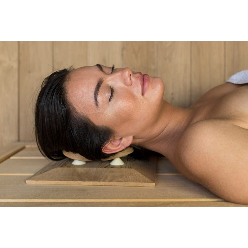 Frau entspannt mit dem ergonomischen Halu Sauna Square Kopfkissen aus Holz in der Sauna