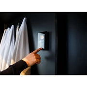 Harvia Club Combi Saunaofen mit Xenio WiFi Steuerung an schwarzer Wand, Hand bedient digitales Display neben weißen Handtüchern