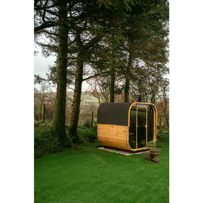 Hekla Cube 160/210/250 Gartensauna mit Holzverkleidung und schwarzem Dach im grünen Garten zwischen Bäumen