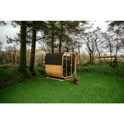 Hekla Cube 160/210/250 Gartensauna mit Holzverkleidung und schwarzem Dach in parkähnlicher Umgebung
