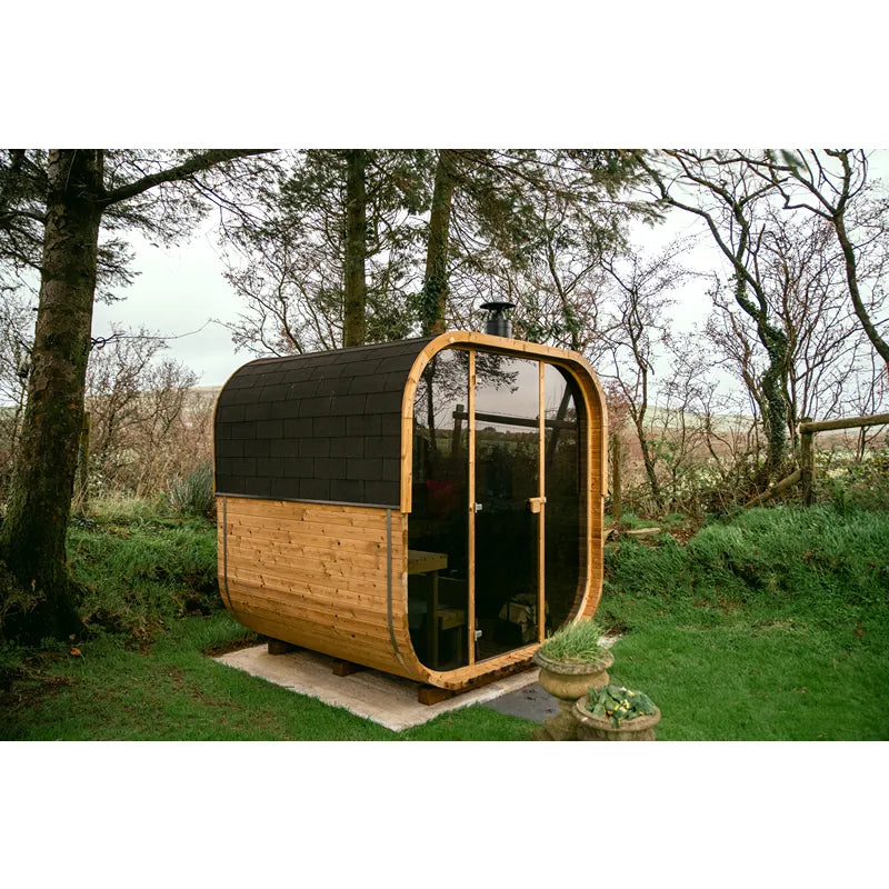 Hekla Cube 160/210/250 Gartensauna mit Holzverkleidung und schwarzem Dach im waldigen Garten