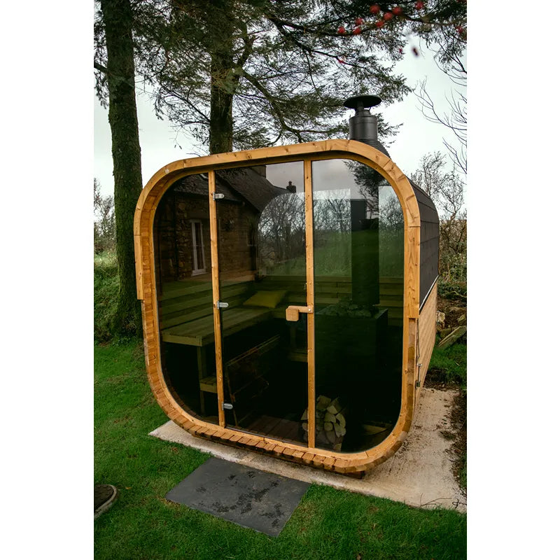 Hekla Cube 160/210/250 Gartensauna mit Holzrahmen und großen Glastüren im Garten aufgestellt