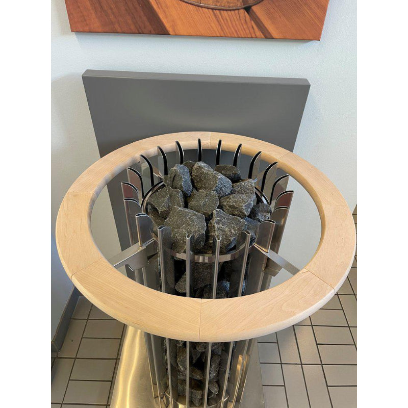 Helo Einbaurahmen aus hellem Holz mit integrierter Relinge für Saunaofen, gefüllt mit grauweißen Saunasteinen und metallischen Heizelementen sichtbar