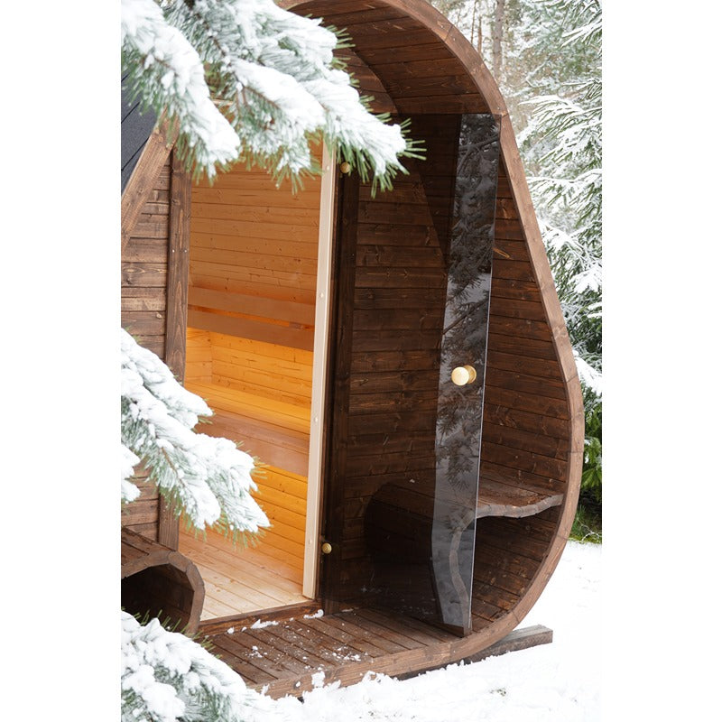 Geöffnete Glastür der Herkus Large Outdoor-Gartensauna in dunkelbrauner Holzoptik mit integriertem Vorraum, Blick ins helle Holz-Innere, umgeben von verschneiter Waldlandschaft.
