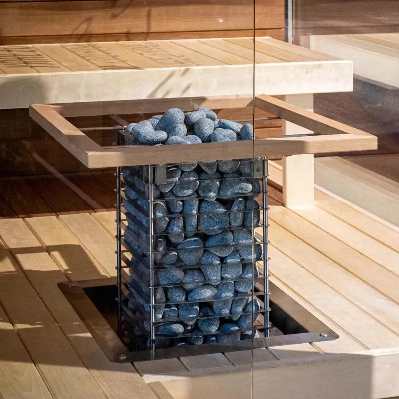 Saunaofen mit Stahlkorb gefüllt mit dunklen Saunasteinen in holzgetäfelter Sauna, Huum Cliff Standofen