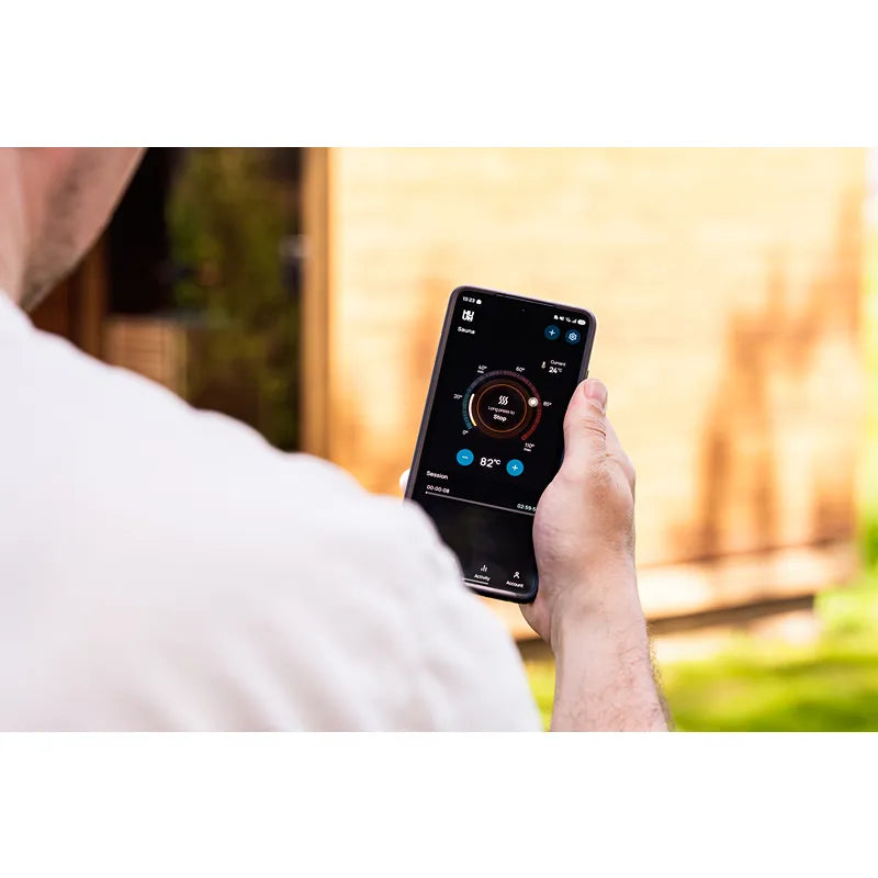 Huum Cliff elektronischer Saunaofen wird per Smartphone-App gesteuert, Mann hält Handy mit Temperaturregelung im Garten