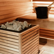Huum Core Black Saunaofen im Inneren einer Holzsauna mit Saunasteinen in Behälter
