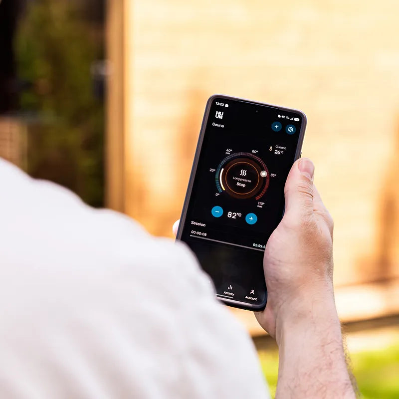 Huum Core Black Saunaofen mit Smartphone-Steuerung, Mann hält Handy mit Sauna-App im Freien