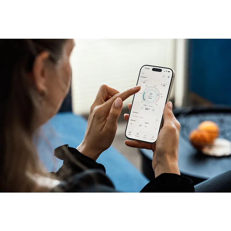 Huum Core Black Saunaofen - Frau bedient die Sauna-Steuerung per Smartphone-App, moderne digitale Kontrolle des elektrischen Standofens