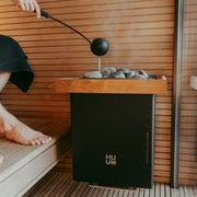 HUUM Core Wall Saunaofen in Schwarz im Sauna-Innenraum mit Aufguss und Holzverkleidung