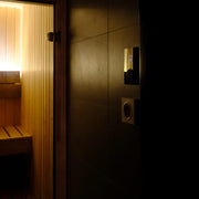 Huum Core Wall Wandofen elektrischer Saunaofen in moderner Saunakabine mit dunkler Verkleidung und Holzbänken