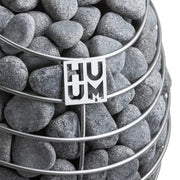 Huum Drop Saunaofen mit grauem Sauna-Steinen in gestapelten Behältern, Huum-Logo auf weißem Etikett sichtbar