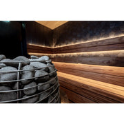 Huum Hive elektrischer Saunaofen mit Saunasteinen in moderner Saunakabine mit Holzbänken und warmer Beleuchtung