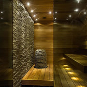 Moderne Saunakabine mit Huum Hive Mini Saunaöfen, Steinwand, Holzbänken und LED-Beleuchtung