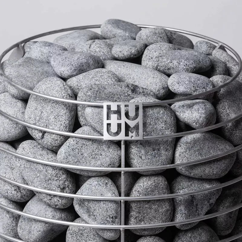 Huum Hive Saunaofen gefüllt mit grauen Saunasteinen in einem Metallkorb mit Huum-Logo