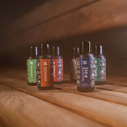 HUUM Saunadüfte Sortiment mit 7 Duftvarianten á 100 ml auf Holzoberfläche, Flaschen mit farbigen Etiketten wie Mango und Mountain Pine