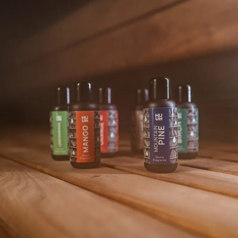 HUUM Saunadüfte Sortiment mit 7 Duftvarianten á 100 ml auf Holzoberfläche, Flaschen mit farbigen Etiketten wie Mango und Mountain Pine