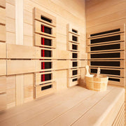 Innenansicht der EAGO AWT Infrarotkabine E1250A-IR mit hellen Hemlock-Holzwänden, mehreren Infrarot-Heizelementen mit roten Leuchtanzeigen und integrierter Holzbank für vier Personen